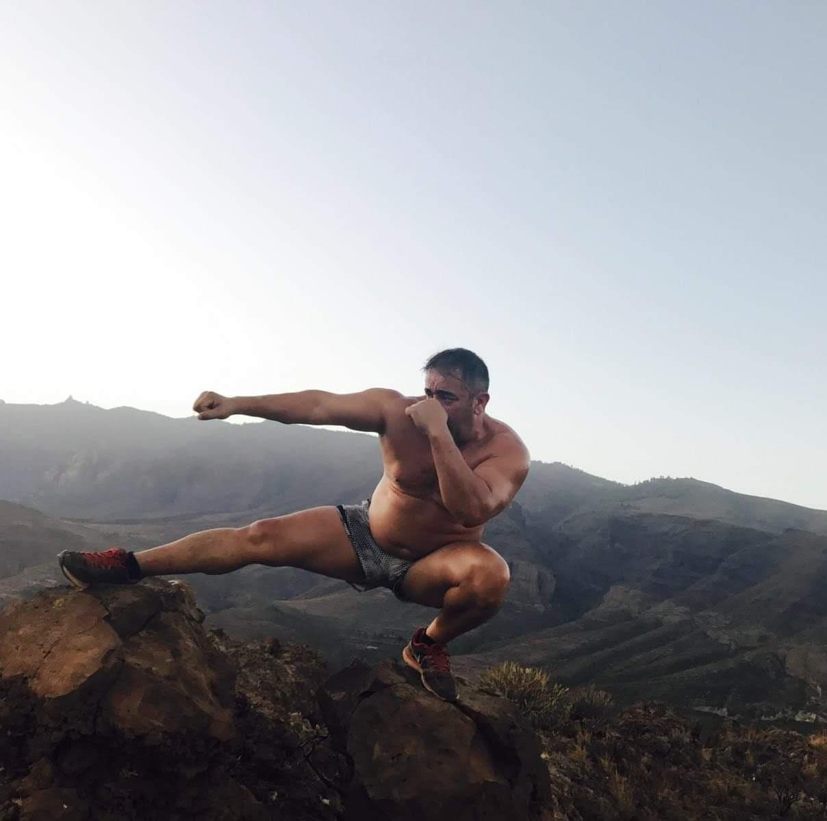 Fernando González Cruz en posición de guardia sobre una roca, con las montañas de Gran Canaria al fondo